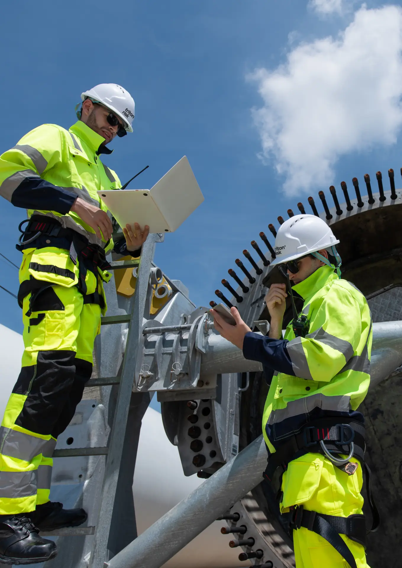 Industrial safety technicians using a portable gas detector and two-way radio beside temporary lighting within a process plant