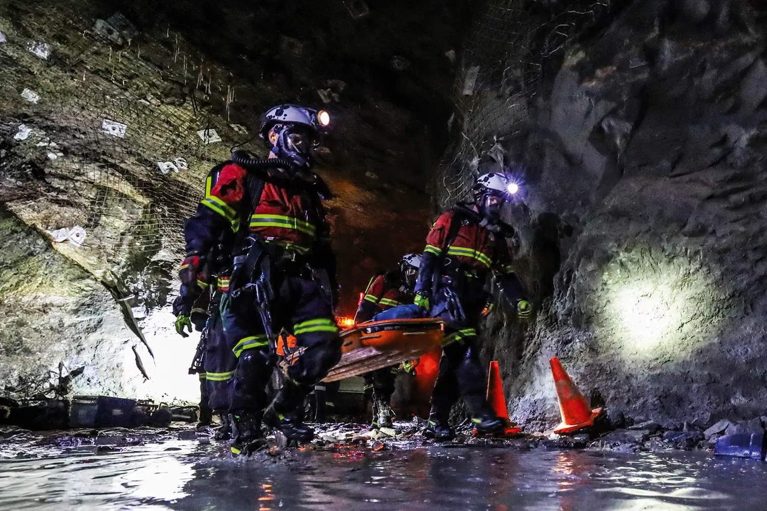 Specialist underground rescue team wearing long-duration breathing apparatus moving a rescue stretcher deep into a tunnel under construction