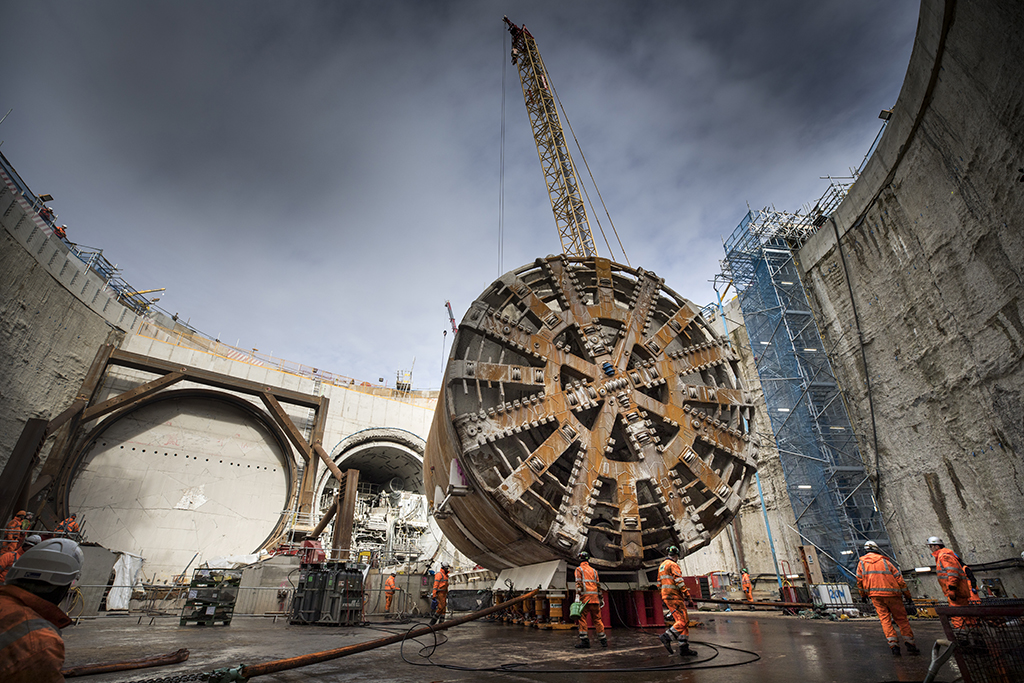 Tunnel boring machine cutterhead in a deep construction shaft with workers in hi-vis PPE — major infrastructure project