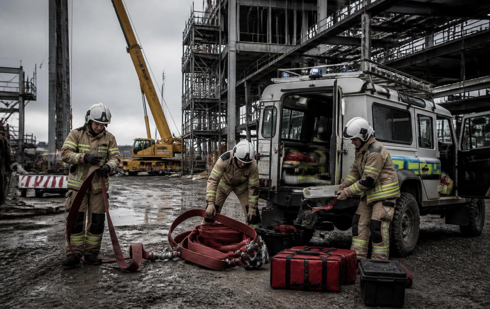 Emergency response team preparing firefighting hose and rescue equipment beside a response vehicle on a major construction site